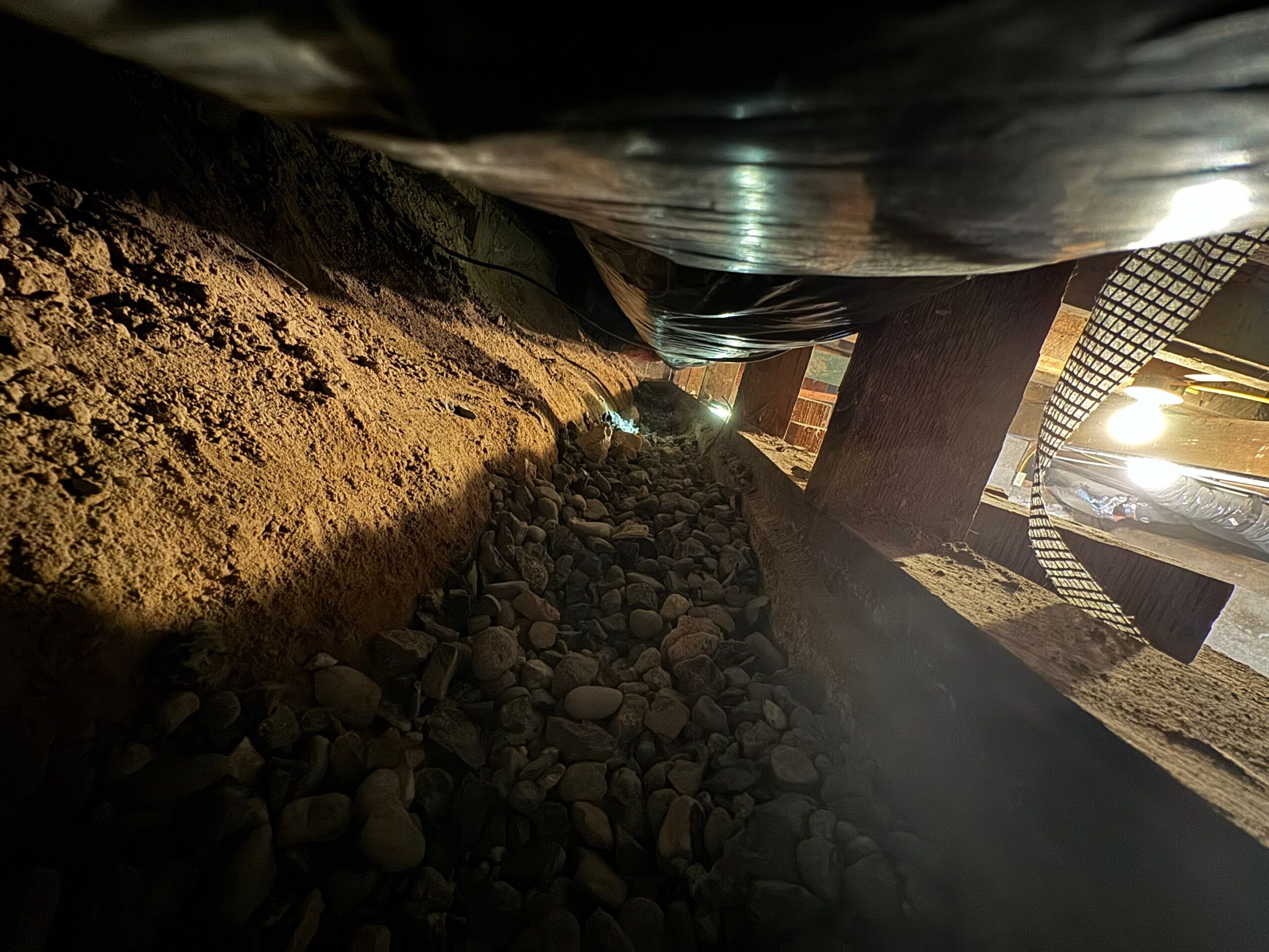 dirt-floor crawl space beneath a home, currently undergoing waterproofing work